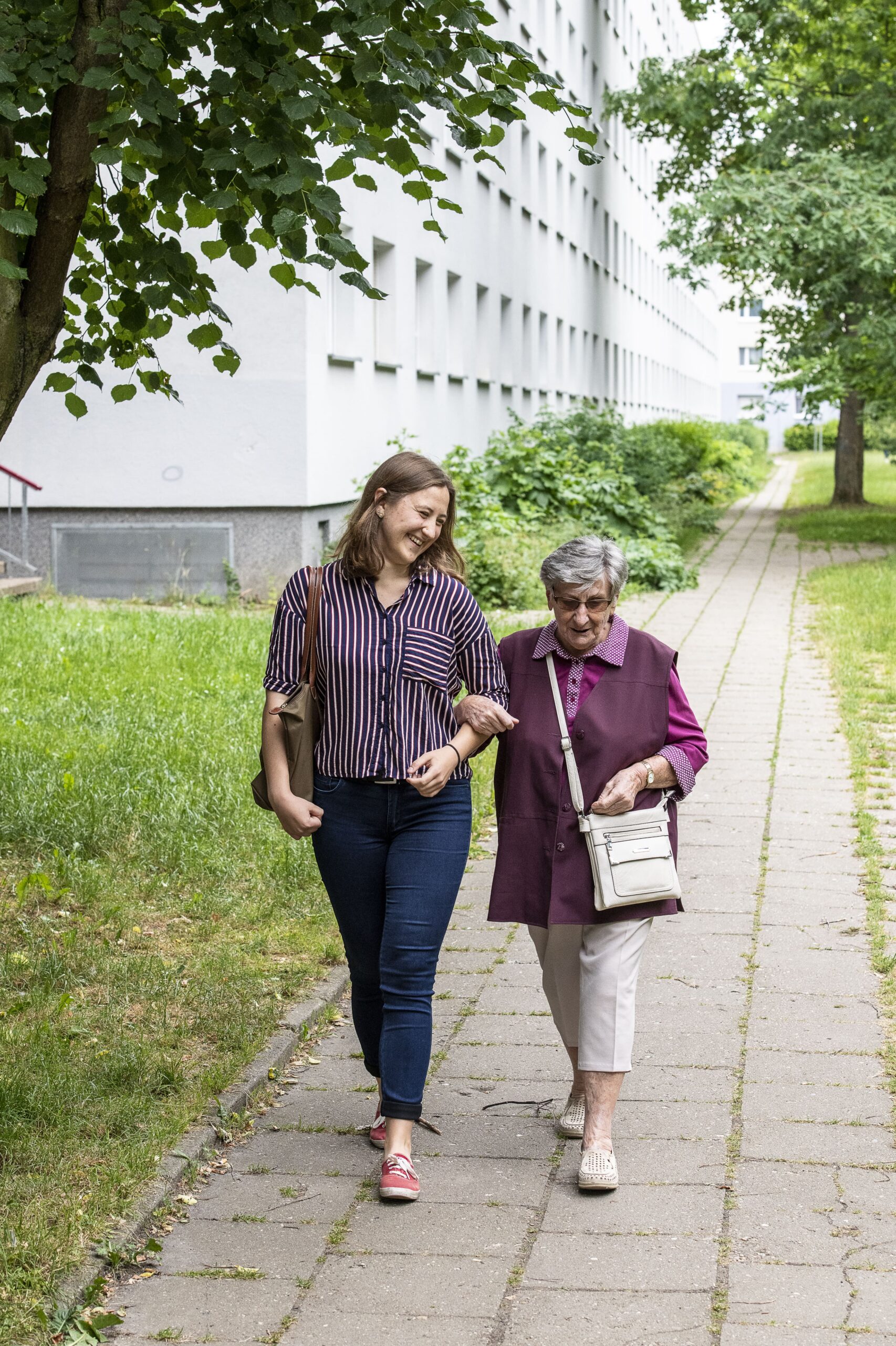 Eine junge Frau und eine ältere Frau laufen eingehakt einen Weg entlang und lächeln